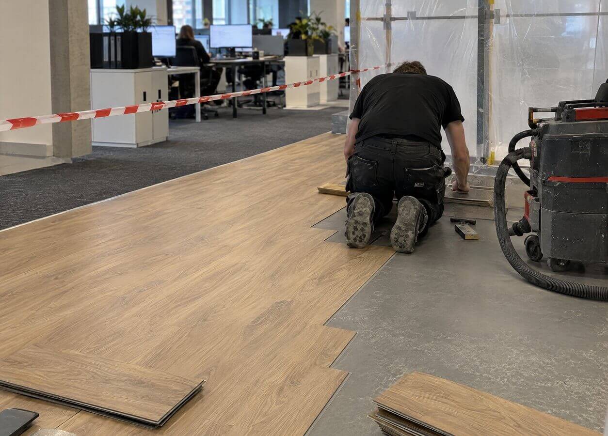 Bodenleger verlegt Vinyl in einem abgetrennten Bereich, während im Büro weitergearbeitet wird